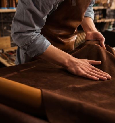 Close up of a male shoemaker working with leather textile at his workshop
